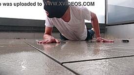 Masked figure masturbates outdoors in wet jeans on a rainy balcony.