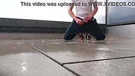 Masked figure masturbates outdoors in wet jeans on a rainy balcony.