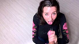 A young woman with large breasts enjoys sucking on a huge piece of candy in a playful manner.