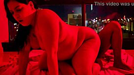 Brunette chubby girl sits on big dick under red light, contrasting her small tits with the intense action.