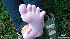 Goddess displays cute curly toes in white socks beneath jeans on spring grass field